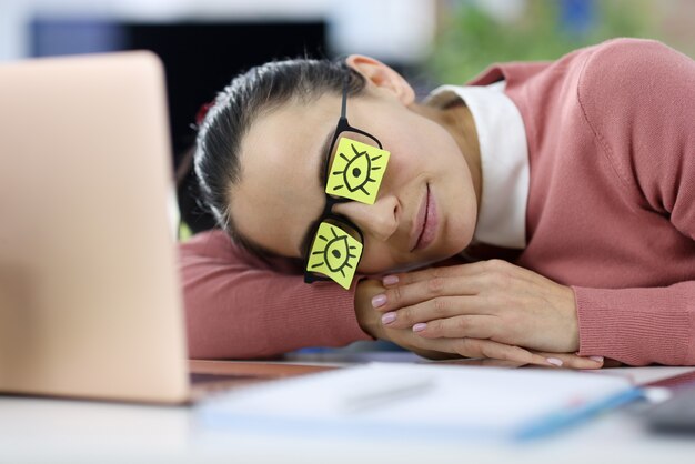 Photo tired woman lies at workplace with stickers on her eyes