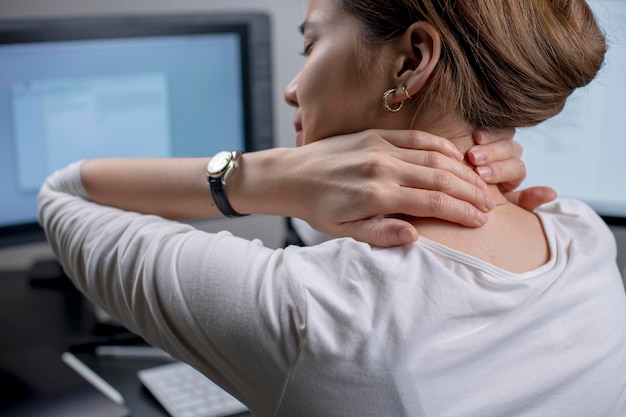 Tired woman massaging rubbing stiff sore neck tensed muscles fatigued from computer work in incorrect posture feeling hurt joint shoulder back pain ache