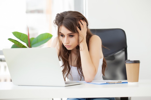 Tired woman in the office working with a laptop.