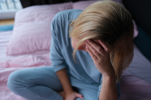 Tired woman in pajamas sitting on the bed closeup