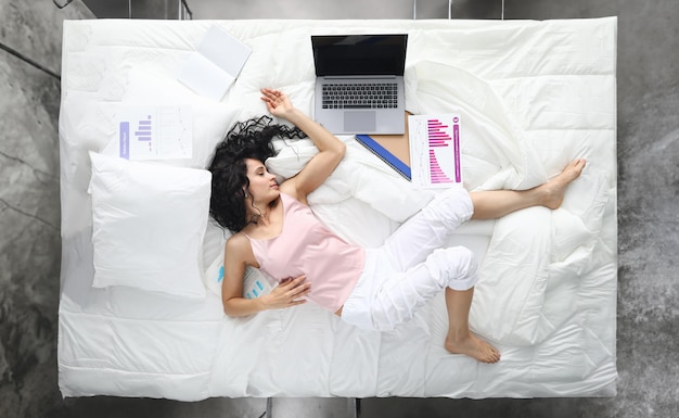 Уставшая женщина в пижаме спит в позе на белой кровати