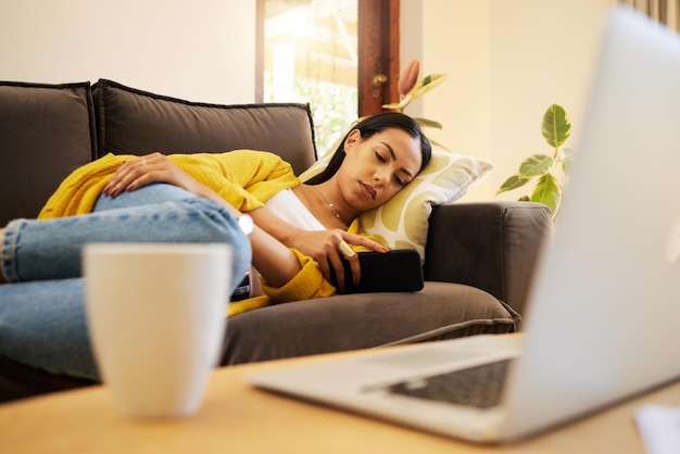 Уставшая женщина звонит по телефону и отдыхает во время рабочего перерыва дома, лежа на диване в гостиной с технологиями