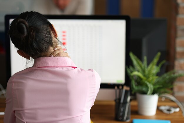 La donna stanca si siede al computer e massaggia il dolore al collo affaticamento e superlavoro in ufficio