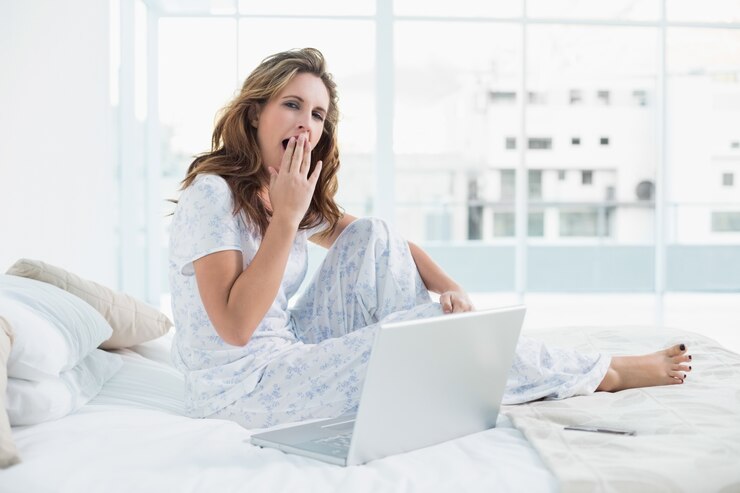 Photo tired woman sitting on cosy bed with laptop