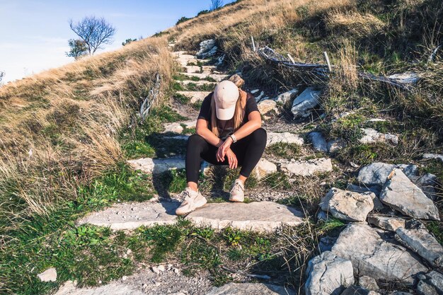 Tired woman sitting on stone steps while climbing to the top of the mountain                                person