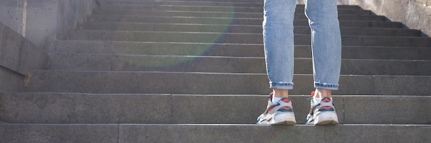 Уставшая женщина в кроссовках, стоящая перед длинной лестницей со ступенями, ходит турист