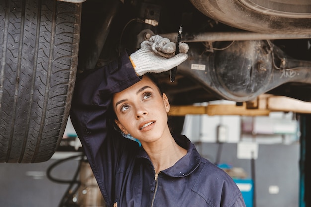 疲れた女性スタッフが自動車のガレージで汗を拭き取る危険な場所で一生懸命働いています。