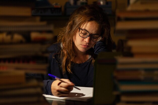 tired woman studying between many books in a library at night