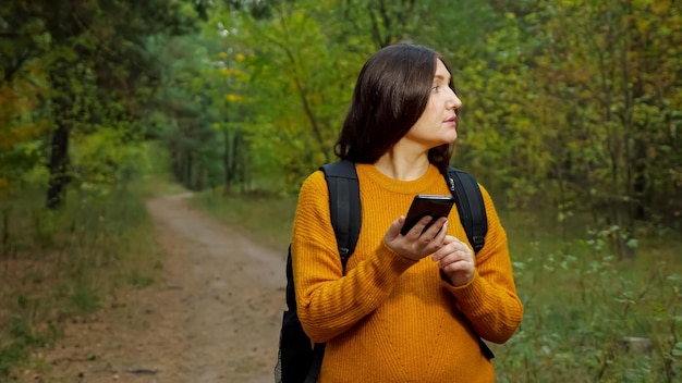 Tired woman tourist reads map on phone walking along forest