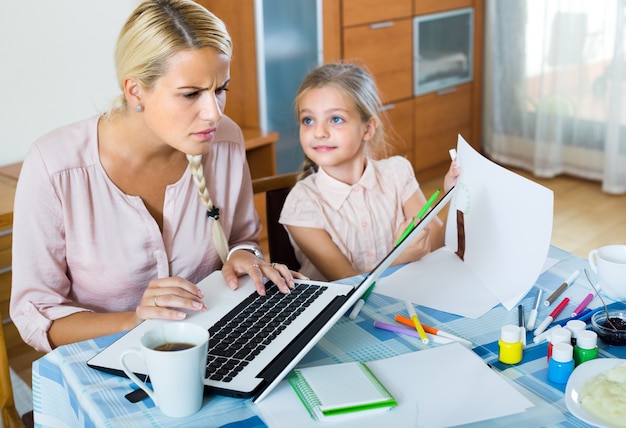 Donna stanca con la figlia che lavora online