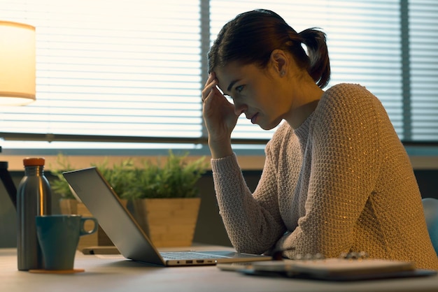 Усталая женщина с головной болью работает с ноутбуком
