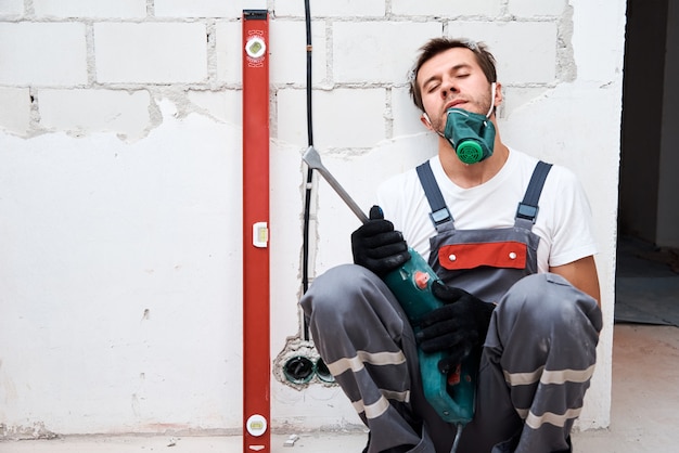 Tired worker man with a hammer drill at construction site