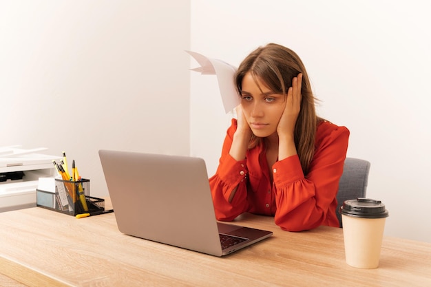 Tired young blonde woman is sitting in the office looking at the computer