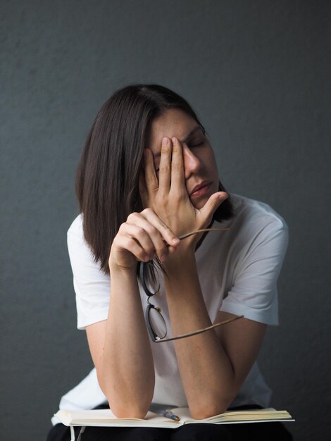 白いTシャツを着た疲れた若い茶色の女性が病気を感じ,長い1日の仕事で頭痛を感じています