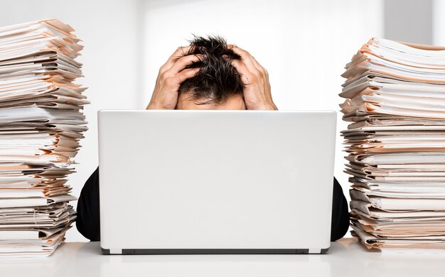 Photo tired young businessman with stack of papers and laptop