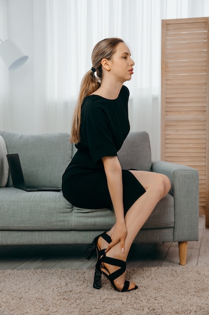 Tired young businesswoman sitting on the sofa and taking off her shoes