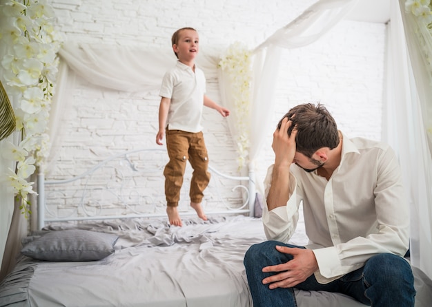 Tired young father is sitting on the edge of bed