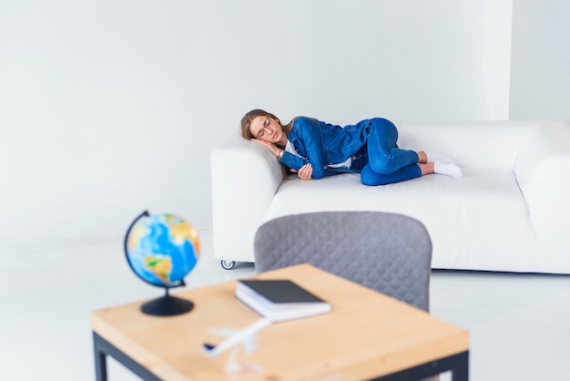 Tired young female student in casual clothing sleeps on white sofa. Beautiful woman resting after hard studying or working day.