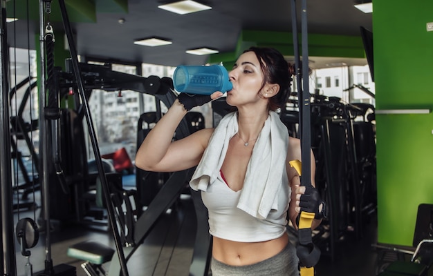 Tired young fit woman drink water in the gym