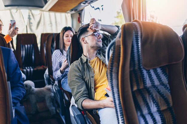 Photo tired young traveler yawning in the bus and listen to music through headphones.