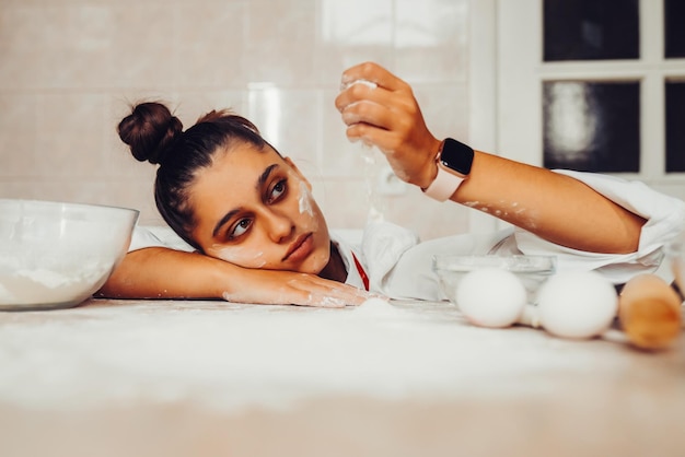 Photo tired young woman is pouring flour on the kitchen table