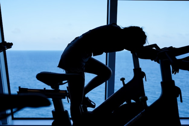 Tired young woman siting on spinning bicycle