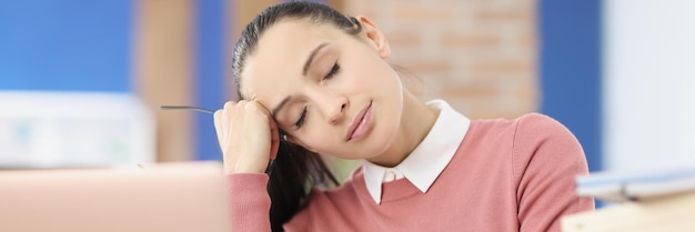 Photo tired young woman sits at workplace with closed eyes overwork at work concept