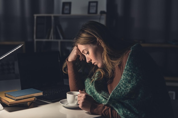 Tired young woman at the workplace wants to sleep late at night