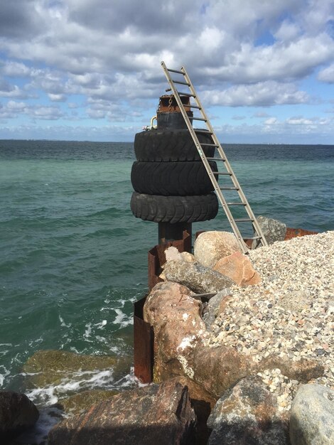 Tires on metallic pole by sea against cloudy sky