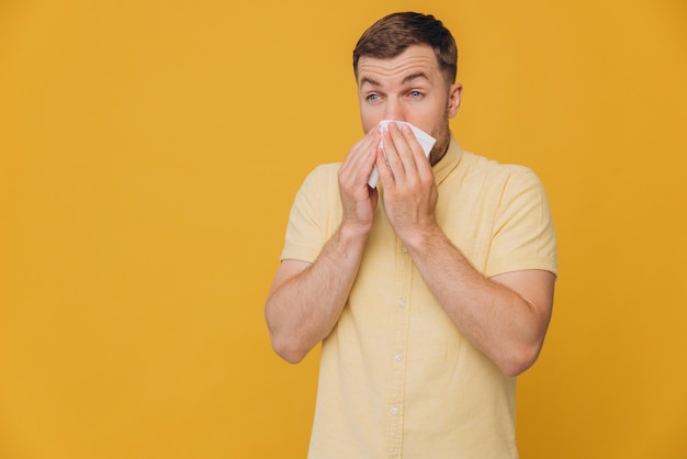 Tissue nose and man in studio for sick allergy cold and influenza on yellow background Bearded male model sneeze wit hayfever allergies and infection of virus bacteria health care and congestion