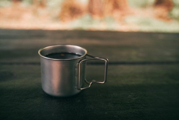 Photo titan metal mug on the wooden table in the forest hike in the woods tea or coffee time while adventure travel in the forest tourism equipment concept