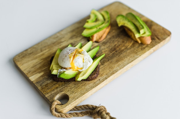 Toast, avacado sandwich and poached egg on a wooden chopping Board.