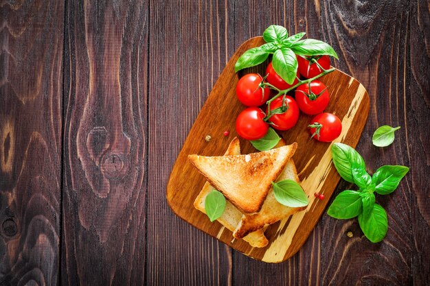 Fette di pane tostato, pomodorini e foglie di basilico su legno