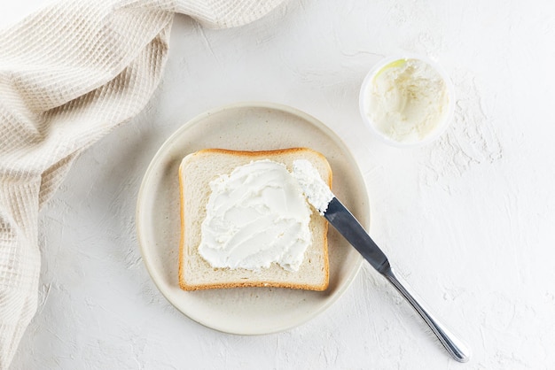 Toast bread spread with cream cheese in a plate on a light table top view