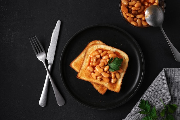 Toast bread with baked beans with parsley on plate on black table top view