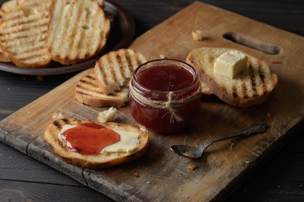 Тостовый хлеб с домашним клубничным джемом и на деревенском столе с маслом на завтрак или поздний завтрак