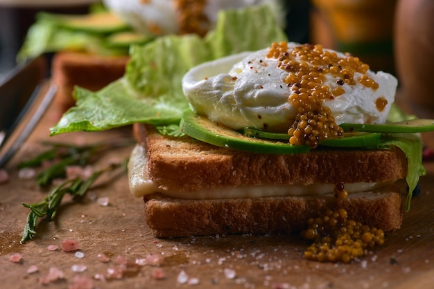 Toast brood met gesneden avocado, zakje ei en Groenen op houten snijplank.