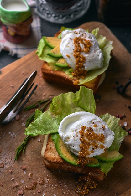 Toast brood met gesneden avocado, zakje ei en Groenen op houten snijplank.