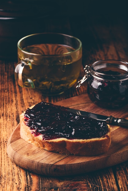 Toast met bessenjam op snijplank en kopje groene thee