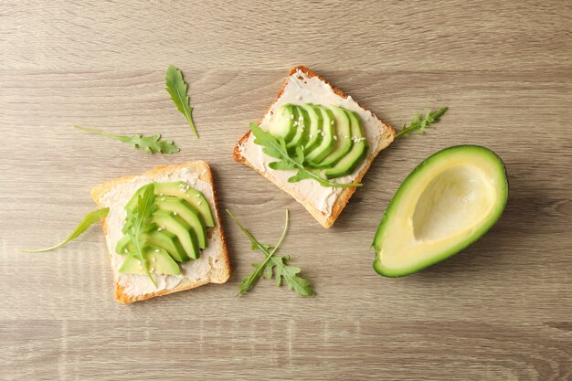 Toast met boter, avocado, rucola en sesam op houten achtergrond, bovenaanzicht