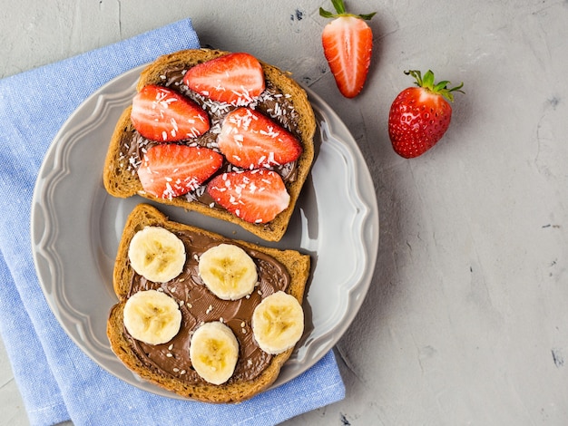 Toast met chocolade en fruit op een grijze plaat. Aardbeien en bananen op stenen keukentafel