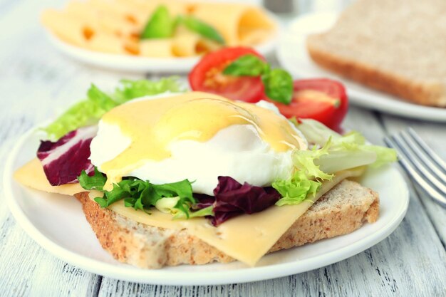 Toast met ei Benedict en tomaat op een bord op een houten tafel.