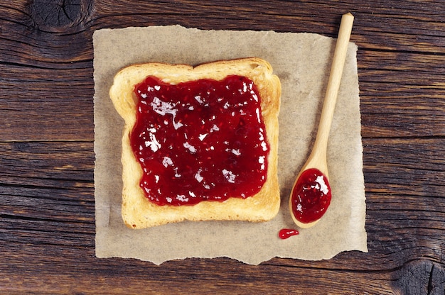 Toast met frambozenjam en lepel op donkere houten tafel. Bovenaanzicht