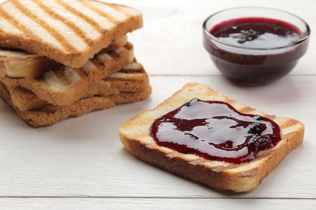 Toast met jam. gebakken knapperige toast met rode jam op een witte houten tafel.