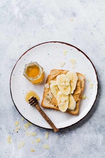 Toast met pindakaas, plakjes banaan, honing en amandelschilfers op een oud grijs beton