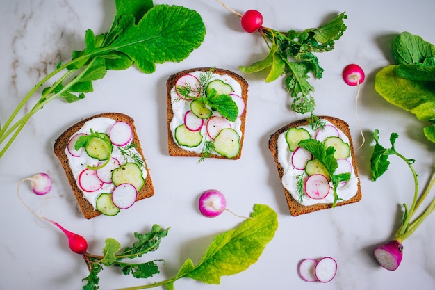 Toast met radijs, komkommer en zwarte sesam van donker brood op een lichte marmeren achtergrond