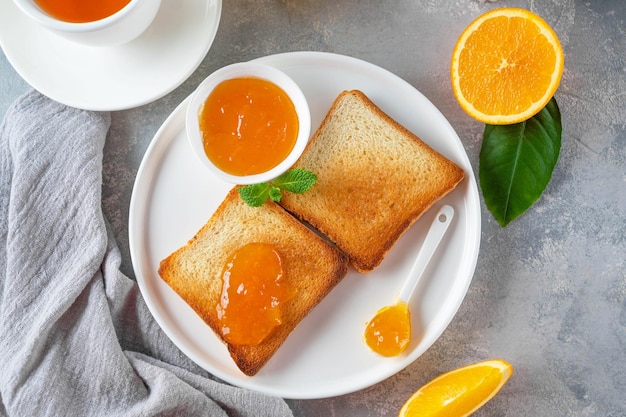 Toast met sinaasappelmarmelade of sinaasappeljam met kopje thee op een grijze achtergrond ruimte kopiëren