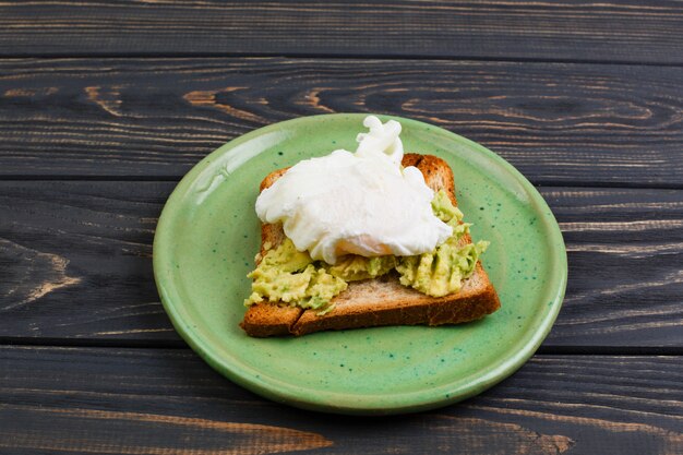 Toast and poached egg with avocado on a green plate on wooden table