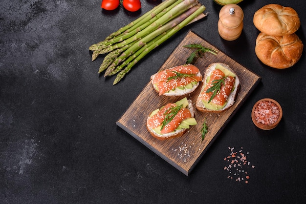 Toast sandwich with butter avocado and salmon decorated with arugula and sesame seeds on a black stone background