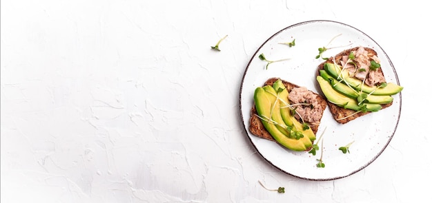 Toast sandwiches met ingeblikte tonijn en avocado op een witte plaat op een lichte achtergrond Lang bannerformaat bovenaanzicht